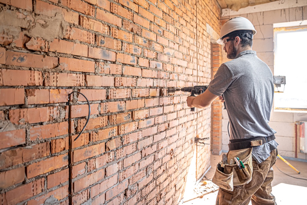Handyman at a construction site in the process of drilling a wall with a perforator.